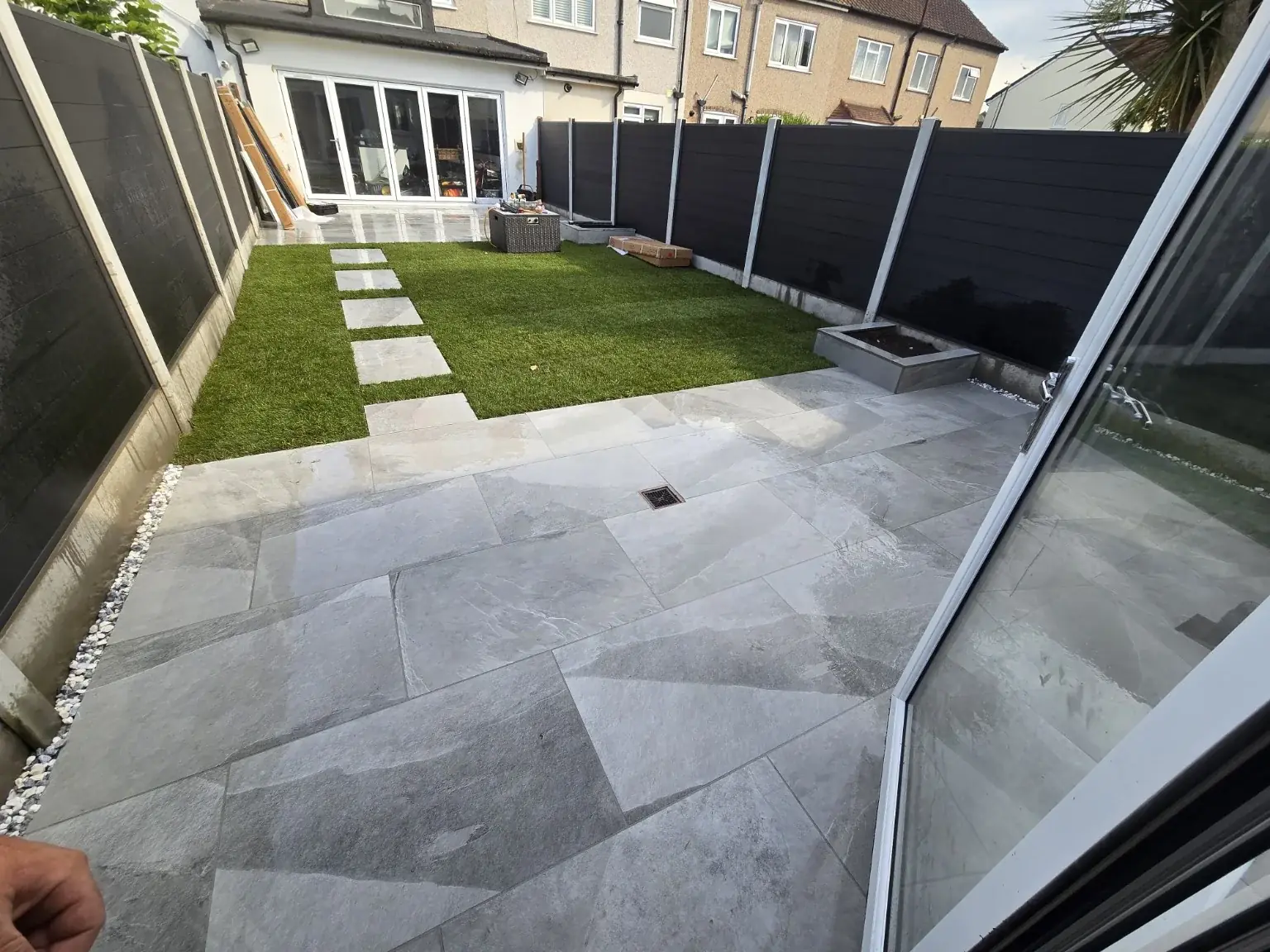 Contemporary landscaped garden with stone paving, lawn and dark fencing