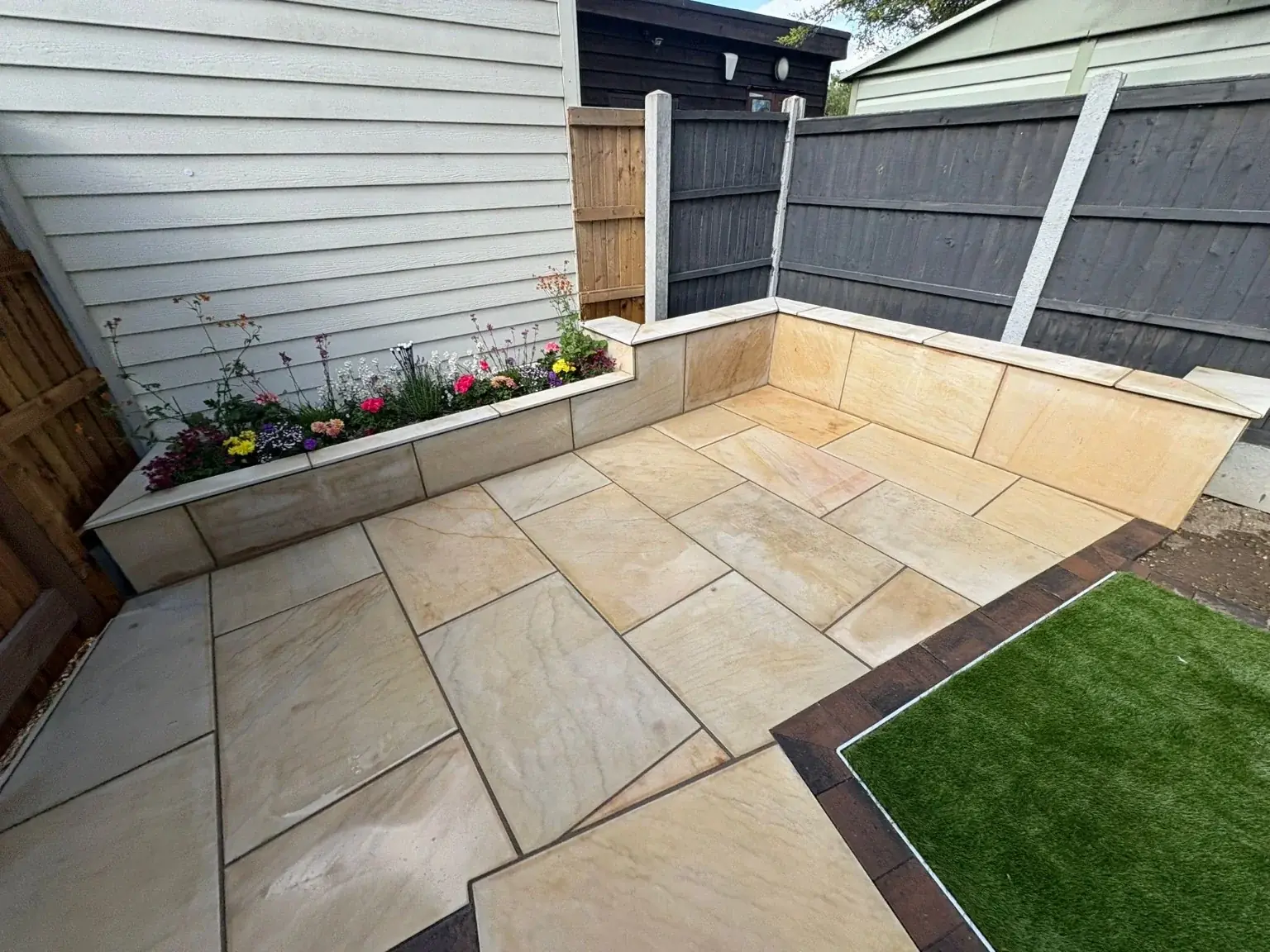 Natural stone patio with a raised flower bed and grey fencing